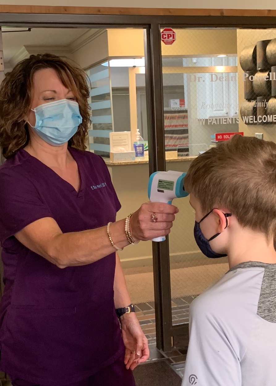 Kimberly is checking in a young patient and taking his temperature before entering the office.